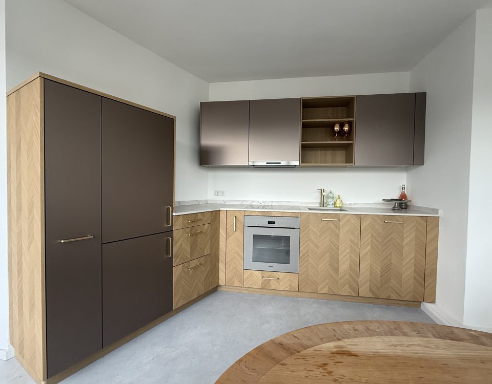 Küche mit Fischgrät-Unterschränken in Eiche, Bronze-Hängeschränken, Dekton-Arbeitsplatte und Einbaugeräten.