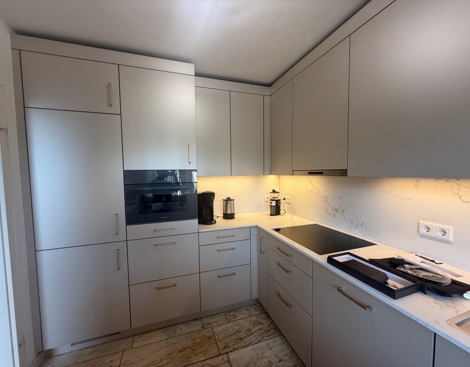 L-Küche mit SMARTGLAS-Fronten in Silk Metallic, Quarzkomposit „Golden Swan“ und Messinggriffen.