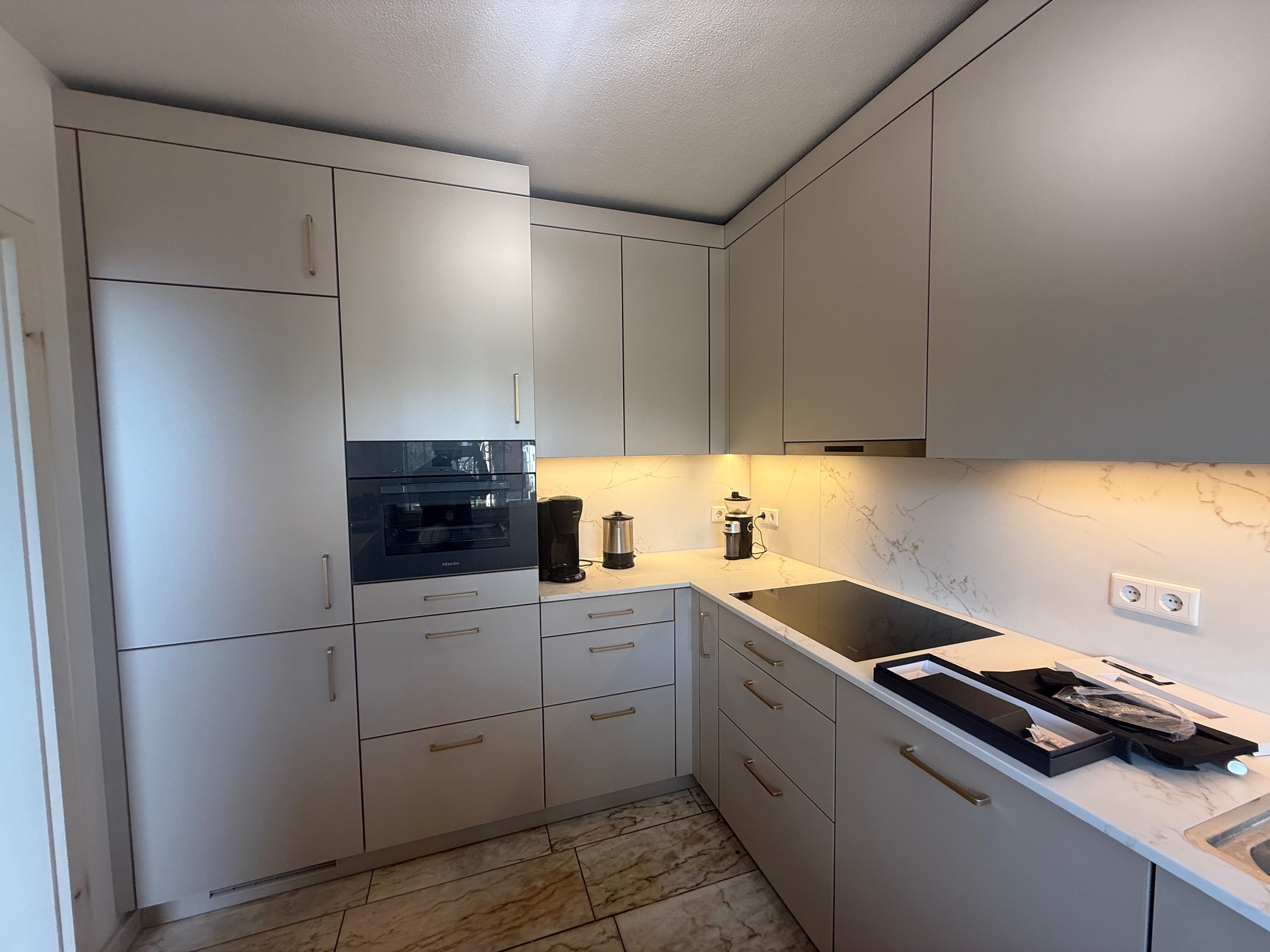 L-Küche mit SMARTGLAS-Fronten in Silk Metallic, Quarzkomposit „Golden Swan“ und Messinggriffen.