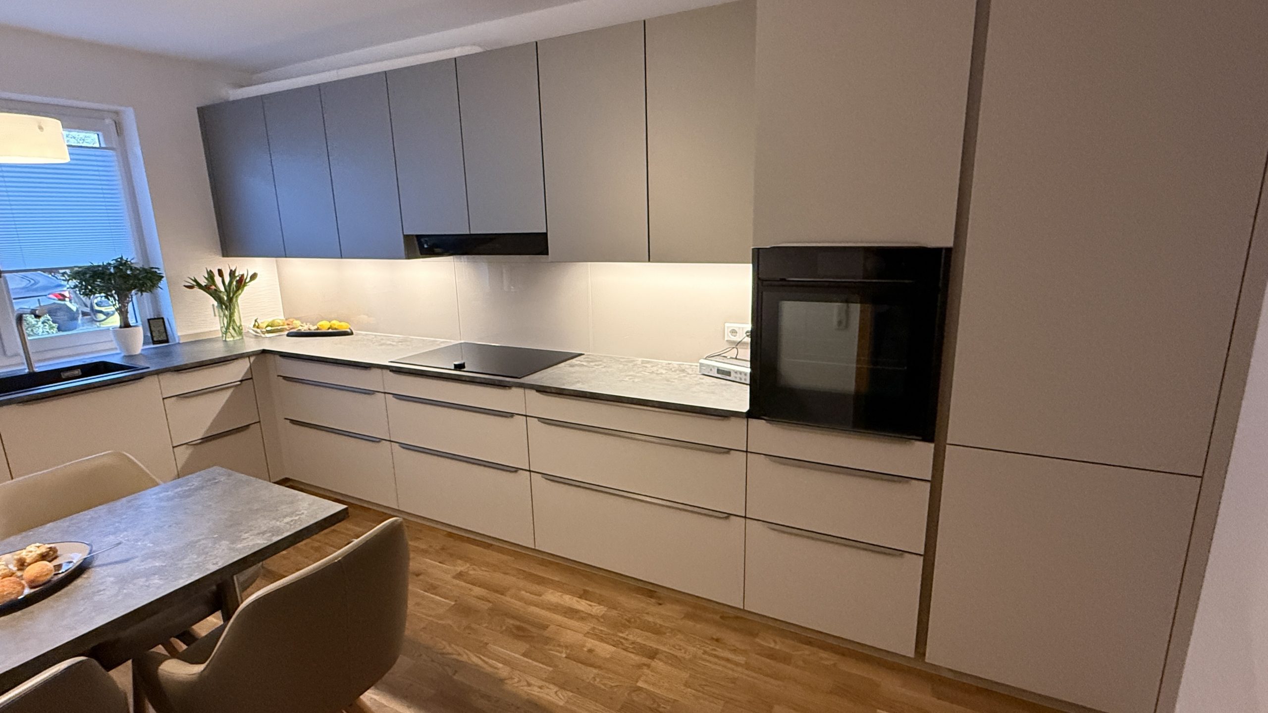 Küchenzeile mit Hochschrank, Dampfbackofen, grauer Arbeitsplatte und weißer Glasrückwand.