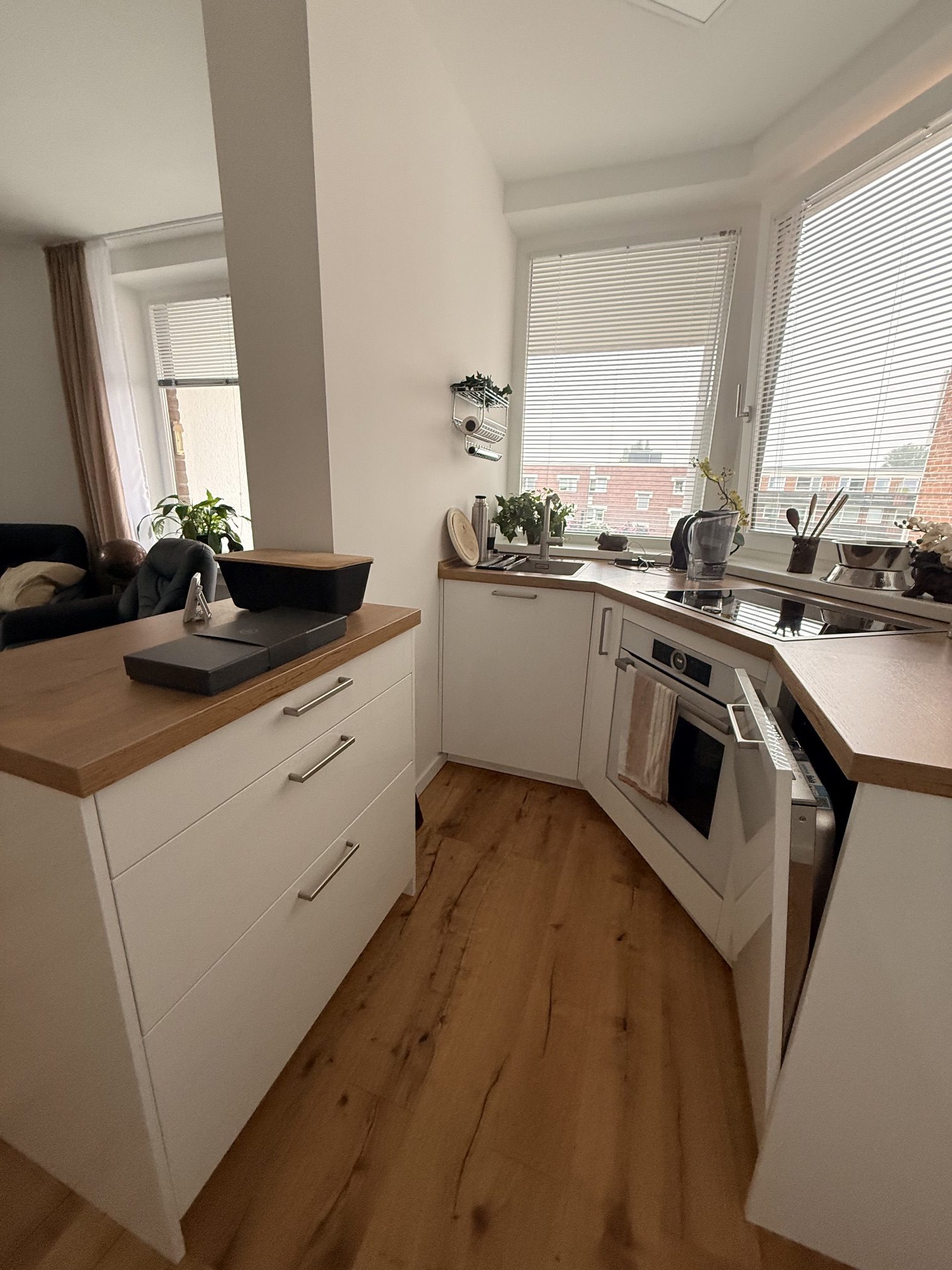 Blick zwischen zusätzlichem Arbeitsblock und weißer U-Küche mit Holzarbeitsplatte und großen Fenstern.