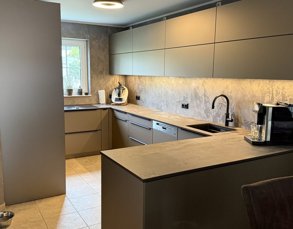 SMARTGLAS Bronze Metallic, Dekton Trilium und schwarze Details verleihen der U-Küche ihre warme, moderne Tiefe.
