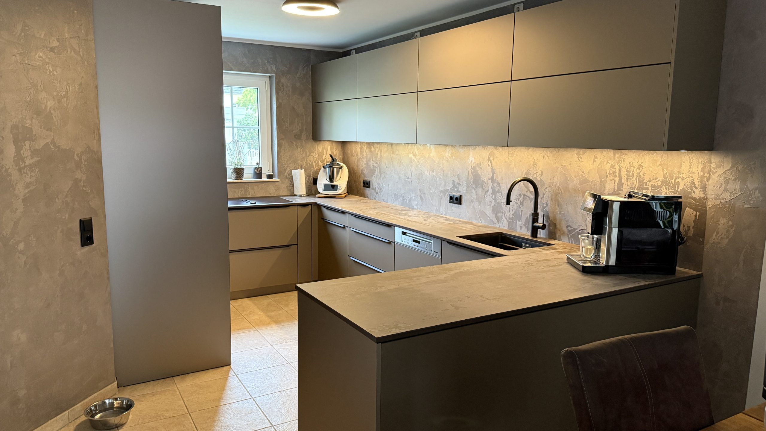SMARTGLAS Bronze Metallic, Dekton Trilium und schwarze Details verleihen der U-Küche ihre warme, moderne Tiefe.