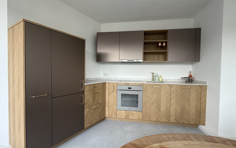 Küche mit Fischgrät-Unterschränken in Eiche, Bronze-Hängeschränken, Dekton-Arbeitsplatte und Einbaugeräten.