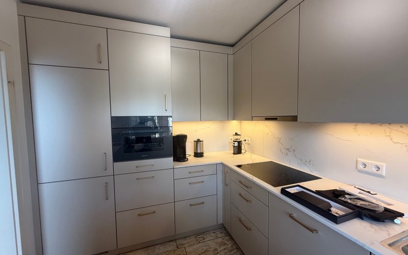 L-Küche mit SMARTGLAS-Fronten in Silk Metallic, Quarzkomposit „Golden Swan“ und Messinggriffen.