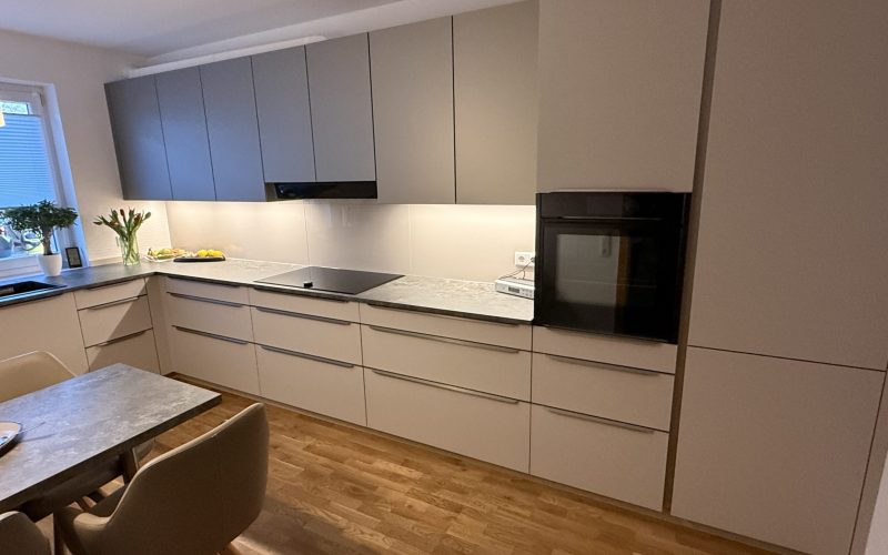 Küchenzeile mit Hochschrank, Dampfbackofen, grauer Arbeitsplatte und weißer Glasrückwand.