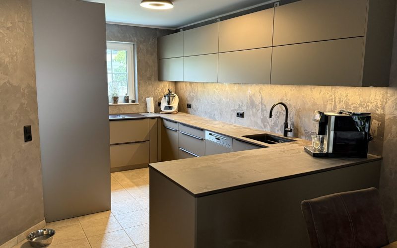 SMARTGLAS Bronze Metallic, Dekton Trilium und schwarze Details verleihen der U-Küche ihre warme, moderne Tiefe.